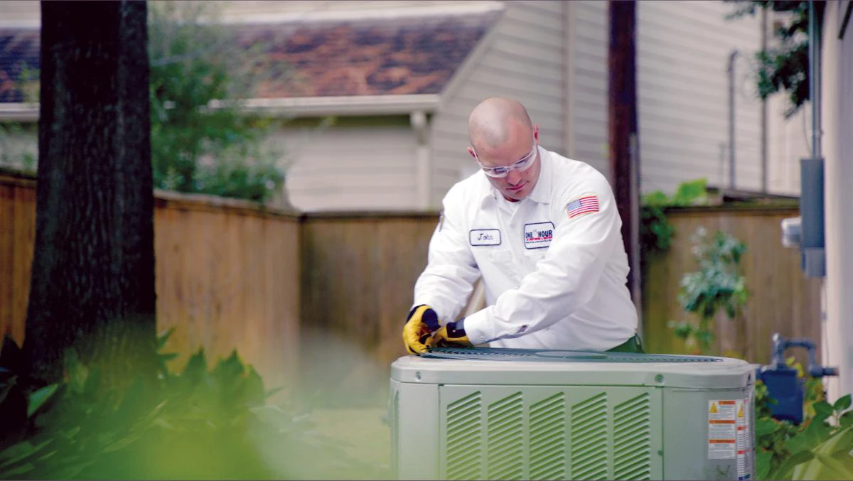 One Hour Heating and Air Conditioning tech, John, working on an outdoor residential AC unit.