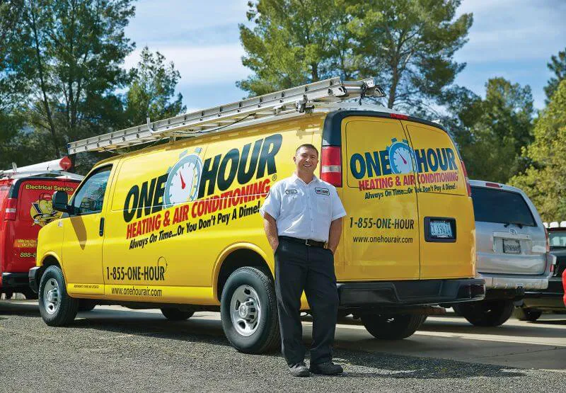 One Hour Heating and Air Conditioning tech standing in front of a wrapped One Hour Heating and Air Conditioning van. 